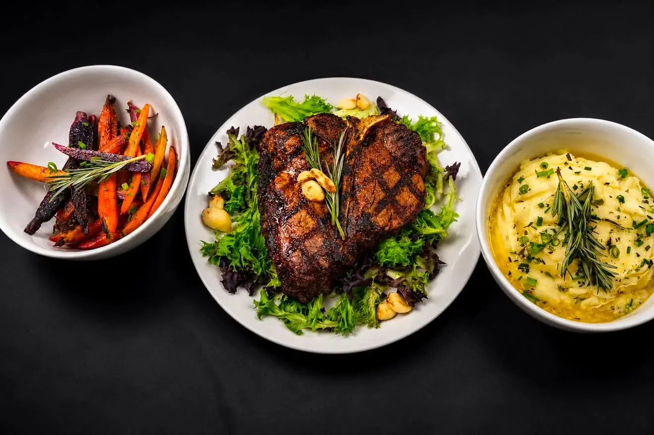 A dry-aged T-bone plated with glazed carrots and rosemary mashed potatoes