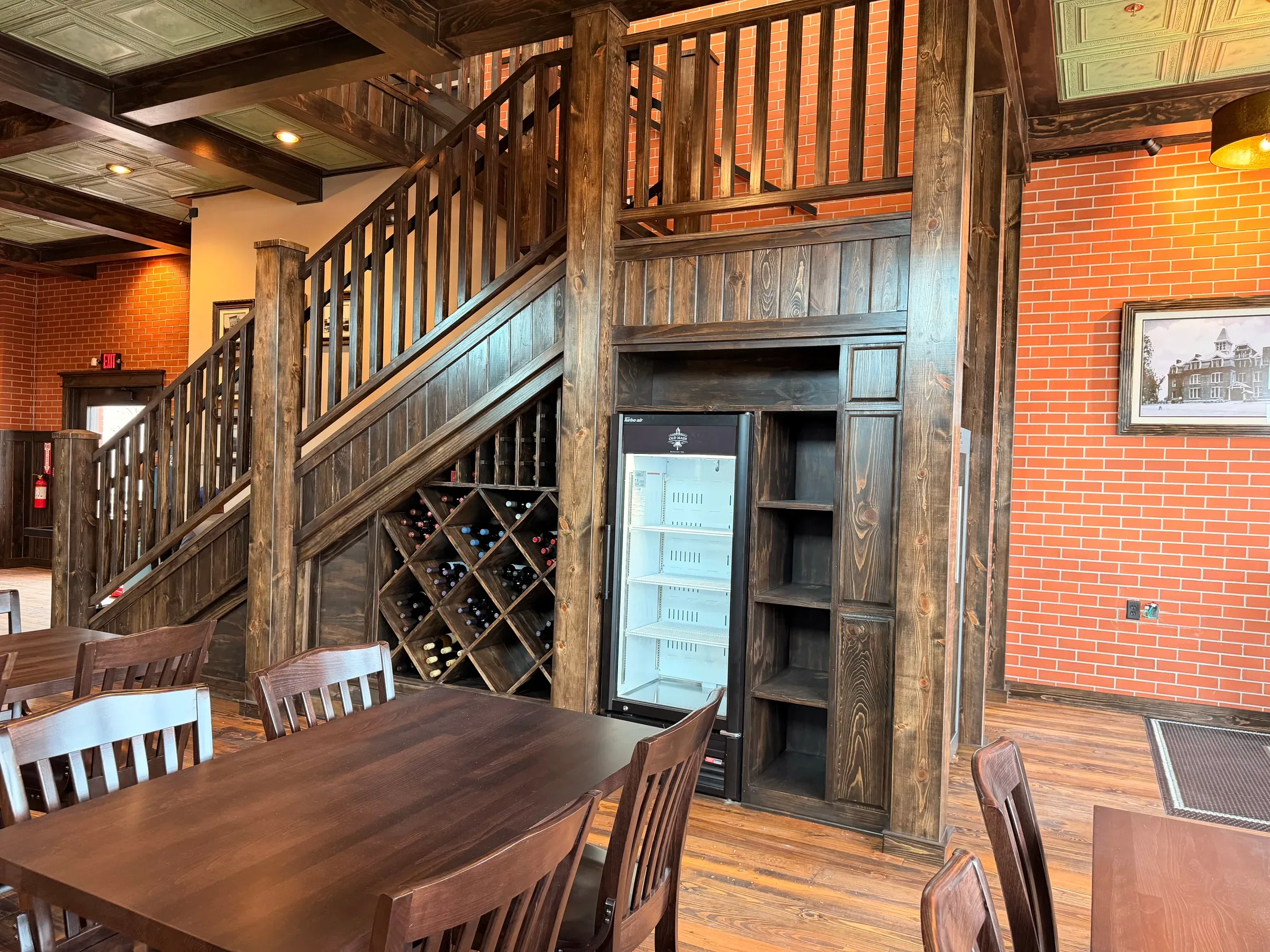 Diamond wine racking and a glass-front wine cooler built in beneath the dining room staircase, framed by heavy timber posts and exposed brick