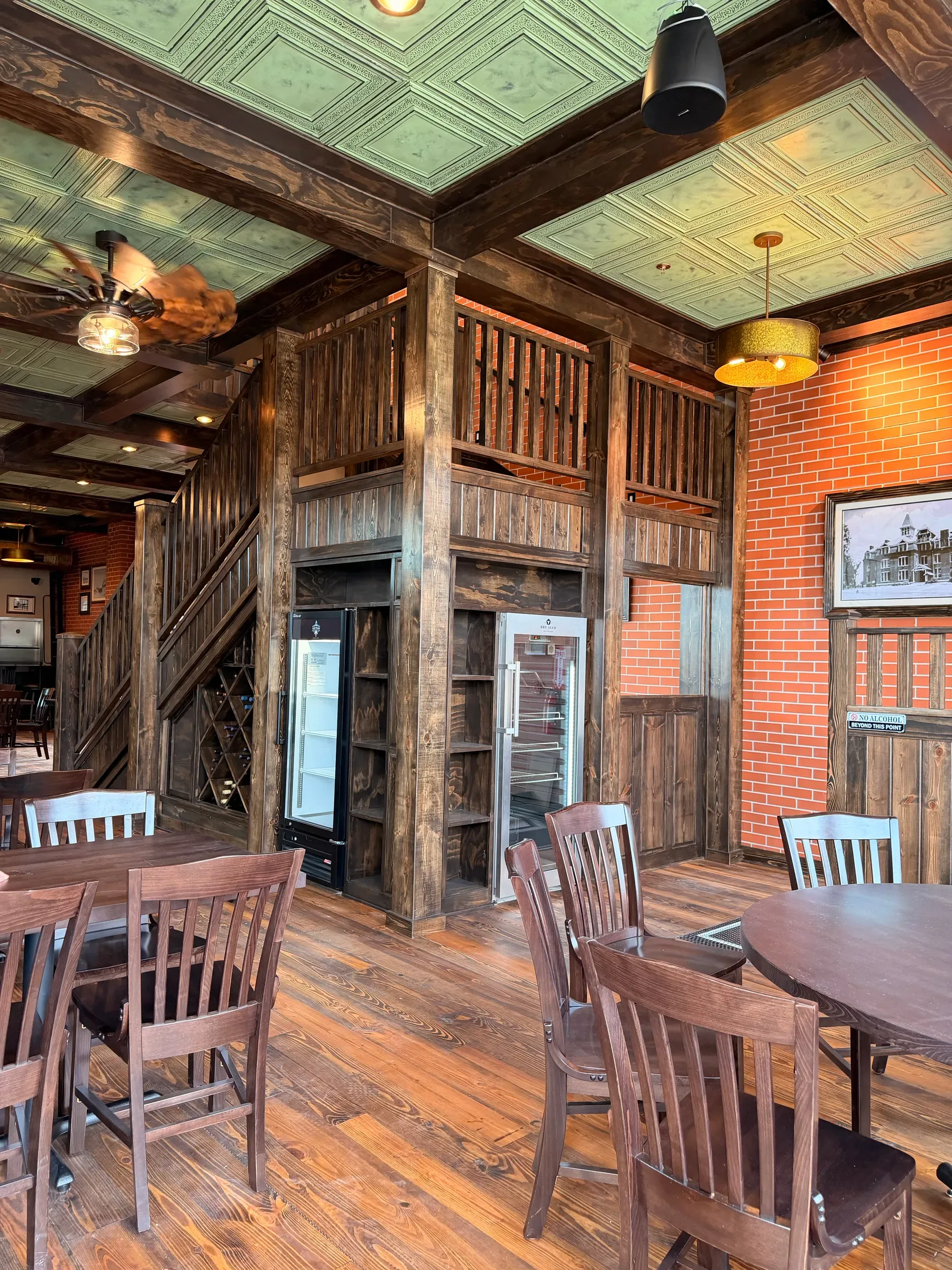 Heavy timber posts and beams framing the dining room, glass-front coolers built into the millwork beneath a green pressed tin ceiling